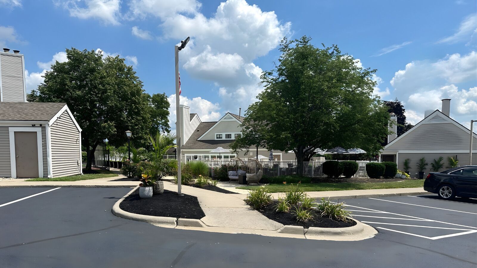 A parking lot with a central landscaped area, a flagpole, and residential buildings in the background.