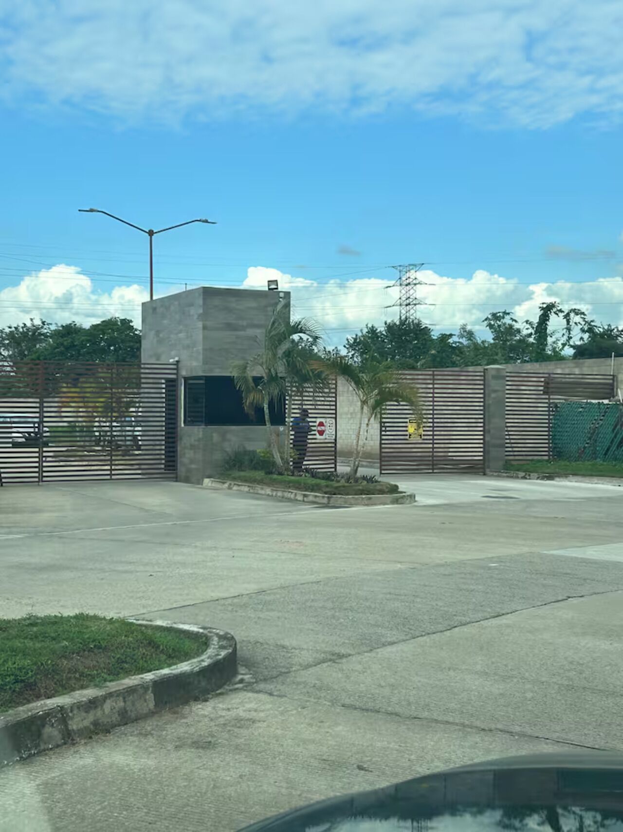 A gated parking area with a concrete building, a street lamp, and a palm tree.