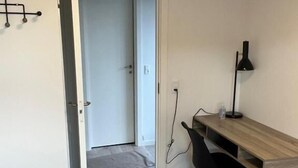 Un dormitorio con cama, escritorio, silla y puerta que da a otra habitación.