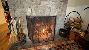 A stone fireplace with a metal grate, a decorative broom, and a rug. - Summer Pocono Cabin Near Skytop Lodge with Fenced Yard; Wkly/Mthly Discounts (Canadensis)