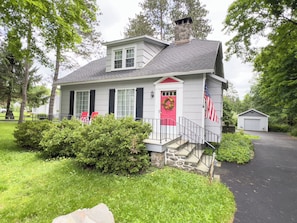 A two-story house with a stone chimney, a red front door, and an American flag. - 5 Bedroom Pocono Cabin Near Skytop Lodge with Fenced Yard  (Canadensis)