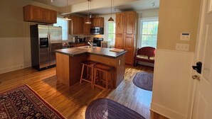 A spacious kitchen with wooden cabinets, a stainless steel refrigerator, and a central island with stools. - Summer Pocono Cabin Near Skytop Lodge with Fenced Yard; Wkly/Mthly Discounts (Canadensis)