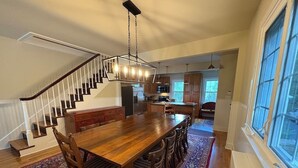 A spacious dining area with a wooden table and chairs, a patterned rug, and a staircase leading to an upper level. - Summer Pocono Cabin Near Skytop Lodge with Fenced Yard; Wkly/Mthly Discounts (Canadensis)