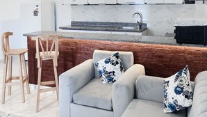 A modern kitchen with white cabinets, a marble countertop, and a built-in oven. There is a grey sofa with floral cushions and a wooden chair. - star- guest house (Luxor Governorate)
