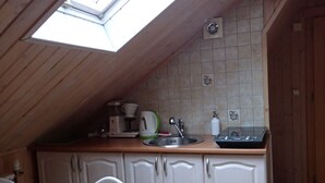 Eine Küche mit schräg verlaufender Decke, einem Oberlicht, weißen Schränken, einer Holz Arbeitsplatte und einem Spülbecken.