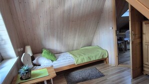 Ein gemütliches Schlafzimmer im Dachgeschoss mit einem Schlafplatz auf Hochbett, einem kleinen Schreibtisch, einem Stuhl und einem Fenster.