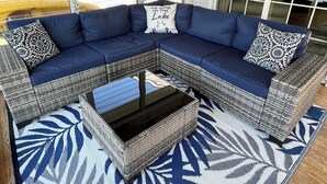 Ein überdachter Außenbereich mit einer blauen Eckcouch, einem gewebten Couchtisch und gemusterten Teppichen.