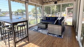 Ein überdachter Außenbereich mit Tisch und Stühlen, einem Deckenventilator und Blick auf Wasser und Boote.