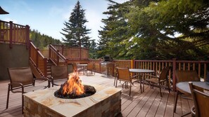 Eine Terrasse im Freien mit einem Steinkamin, Holzstühlen und Tischen, umgeben von einem Hollerdgeschoss und Bäumen.