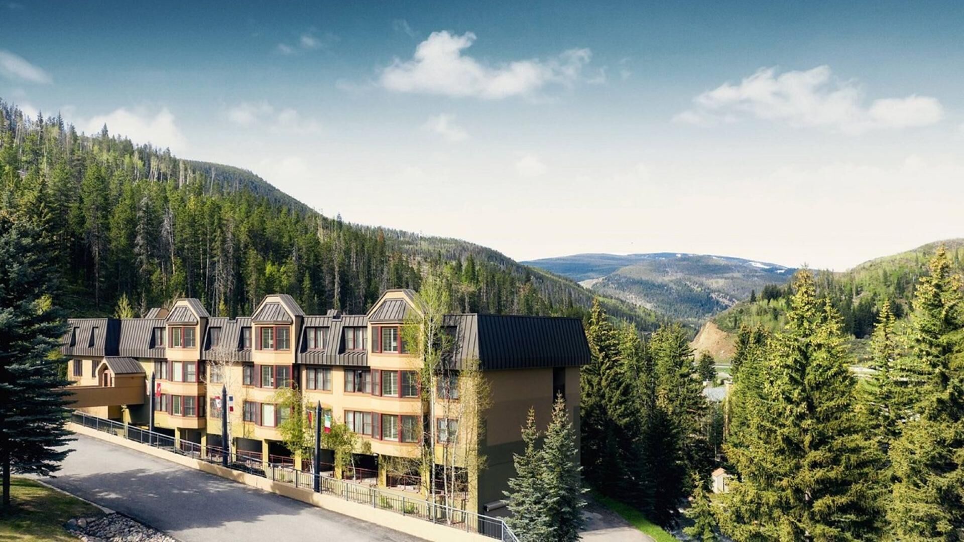 Un hôtel comprenant plusieurs bâtiments, une route asphaltée et un paysage montagneux avec de vastes forêts.
