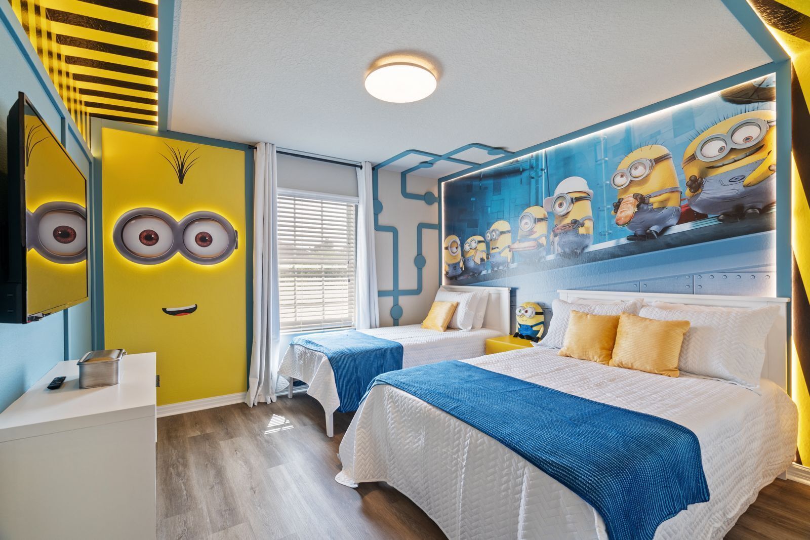 A hotel room with a Minion-themed mural, two beds, a desk, and a mirror.
