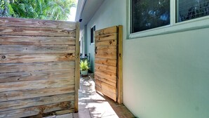 Una puerta de madera que da a una casa con patio de baldosas y una planta en maceta.