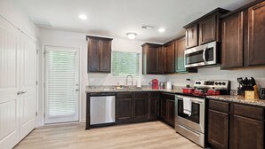 A modern kitchen with dark wood cabinets, stainless steel appliances, and a light wood floor.