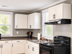 A kitchen with white cabinets, a black stove, and a window with blinds. - Waterfront Beaufort Home - Marsh Views & Screened Porch! (Beaufort)