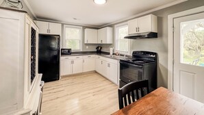 A kitchen with white cabinets, a black refrigerator, a stove, and a wooden dining table.