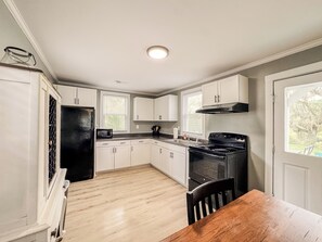 A kitchen with white cabinets, a black refrigerator, a stove, and a wooden dining table.