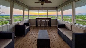 A covered porch with wicker furniture, a table, and chairs, overlooking a green landscape.
