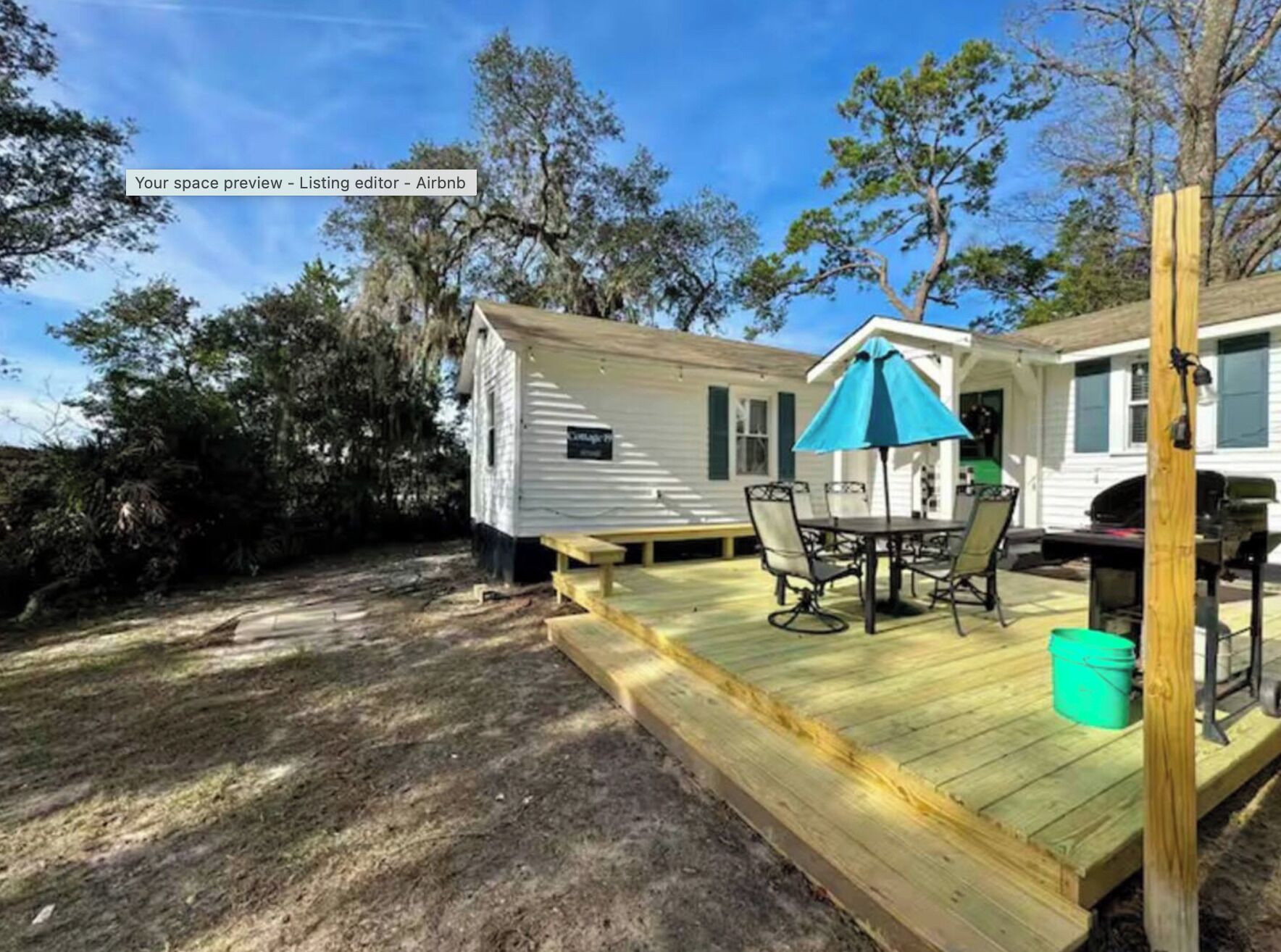 A small house with a wooden deck, a table with chairs, and a blue umbrella.