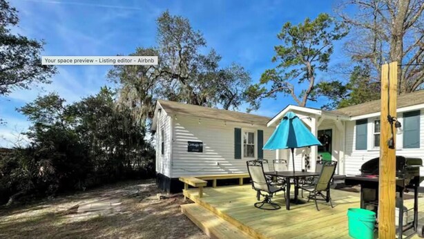 A small house with a wooden deck, a table with chairs, and a blue umbrella.