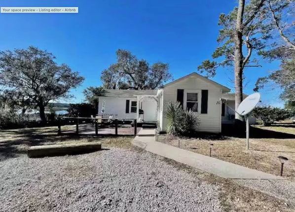 A single-story house with a front porch, a satellite dish, and a gravel driveway.