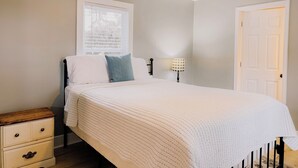 A bedroom with a bed, a nightstand, a lamp, a ceiling fan, and a window.