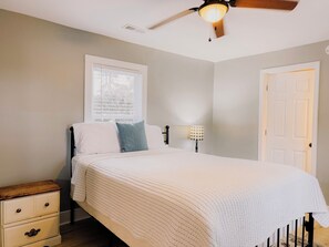 A bedroom with a bed, a nightstand, a lamp, a ceiling fan, and a window.