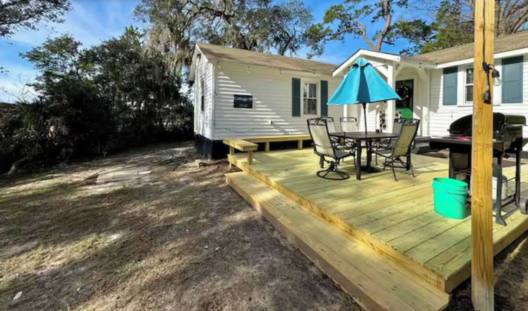 A small house with a wooden deck, a table with chairs, and a blue umbrella.