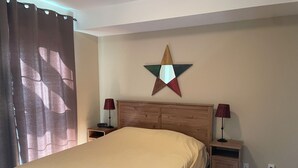 A bedroom with a wooden bed, two bedside tables, a star decoration on the wall, and a curtain on the window.