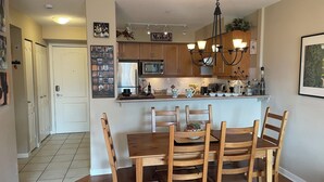 A kitchen with wooden cabinets, a central island with chairs, a chandelier, and various kitchen appliances.