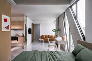 Ett modernt hotellrum med en säng, ett skrivbord, en soffa och utsikt genom stora fönster.