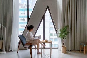 Une chambre moderne avec une grande fenêtre, une chaise, une petite table et une plante en pot.