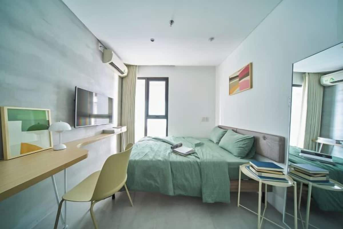 Ein modernes Hotelzimmer mit einem Bett, einem Schreibtisch, einem Stuhl und einem kleinen Tisch mit Büchern.