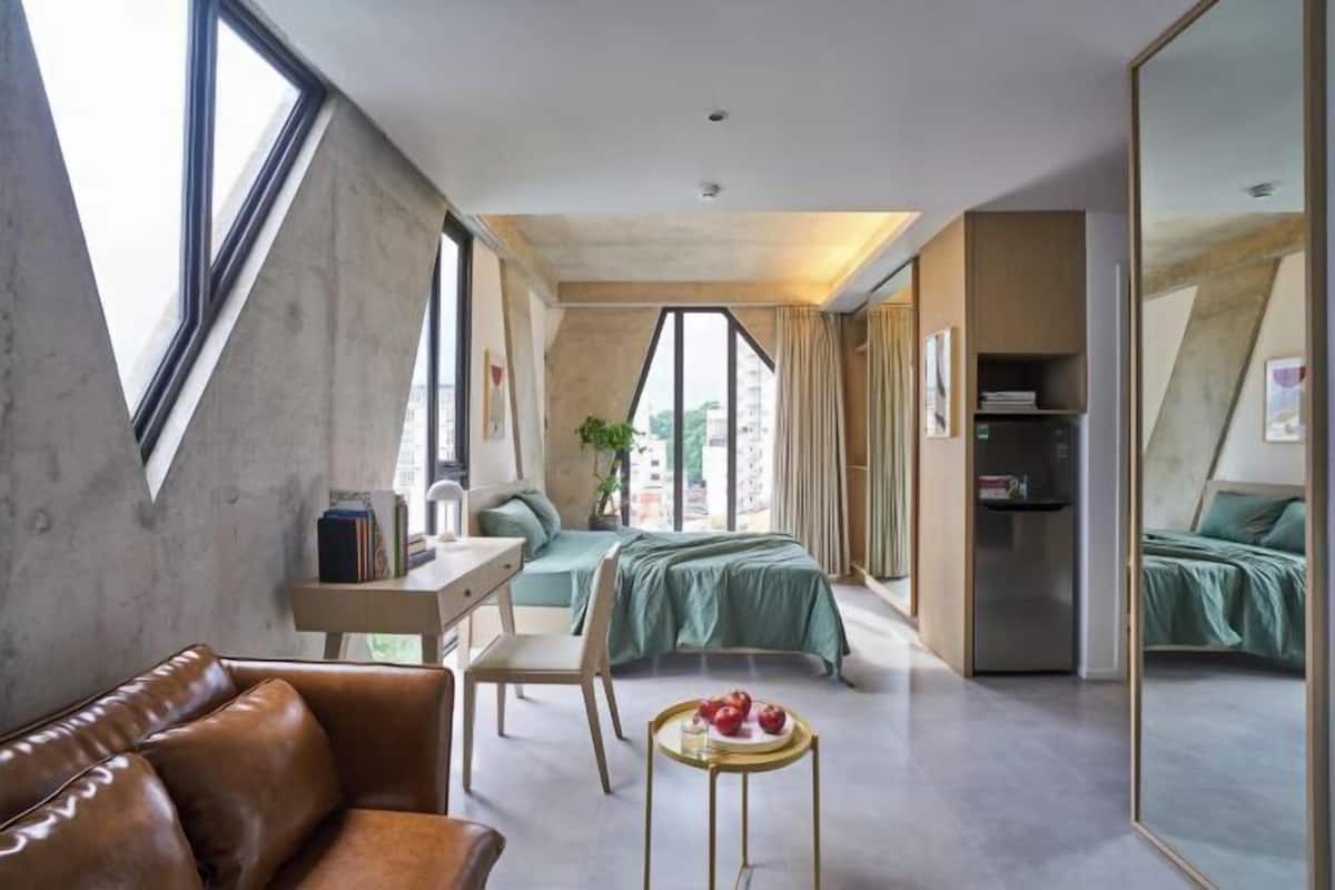 Ein modernes Hotelzimmer mit Schlafbox, Schreibtisch, Ledersofa und Esstisch mit Obst.