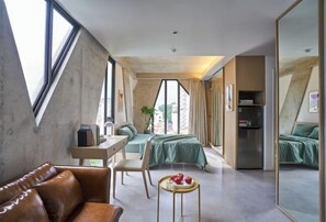 Ett modernt hotellrum med en säng på entresolplan, ett skrivbord, en soffa i läder och ett matbord med frukt.
