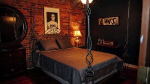 A bedroom with a brick wall, a bed with a headboard, a mirror, a lamp, and a framed poster. - Broadway Penthouse: Stadium View (Nashville)