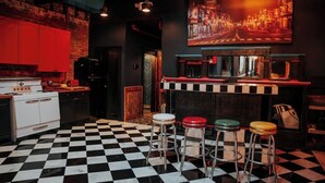 A bar area with a checkered floor, stools, a bar counter, and a painting of a cityscape. - Broadway Penthouse: Stadium View (Nashville)