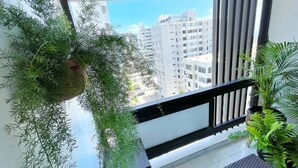 Uma varanda com plantas penduradas, vista de prédios altos e um corrimão.