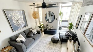 Uma sala de estar moderna com um sofá cinza, um tapete estampado, um espelho redondo e um ventilador de teto.