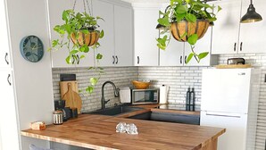 Uma cozinha moderna com ilha central, banquetas, plantas penduradas e micro-ondas.