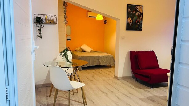 A room with a bed, a red chair, a table with chairs, and a hanging plant. - Cacao House (Capesterre-Belle-Eau)