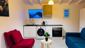 A compact living space with a kitchenette, a red chair, a blue sofa, and a small table with a plant. - Cacao House (Capesterre-Belle-Eau)