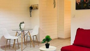 A modern living room with a white brick wall, a red sofa, a blue couch, and a dining area with a glass table and white chairs. - Cacao House (Capesterre-Belle-Eau)