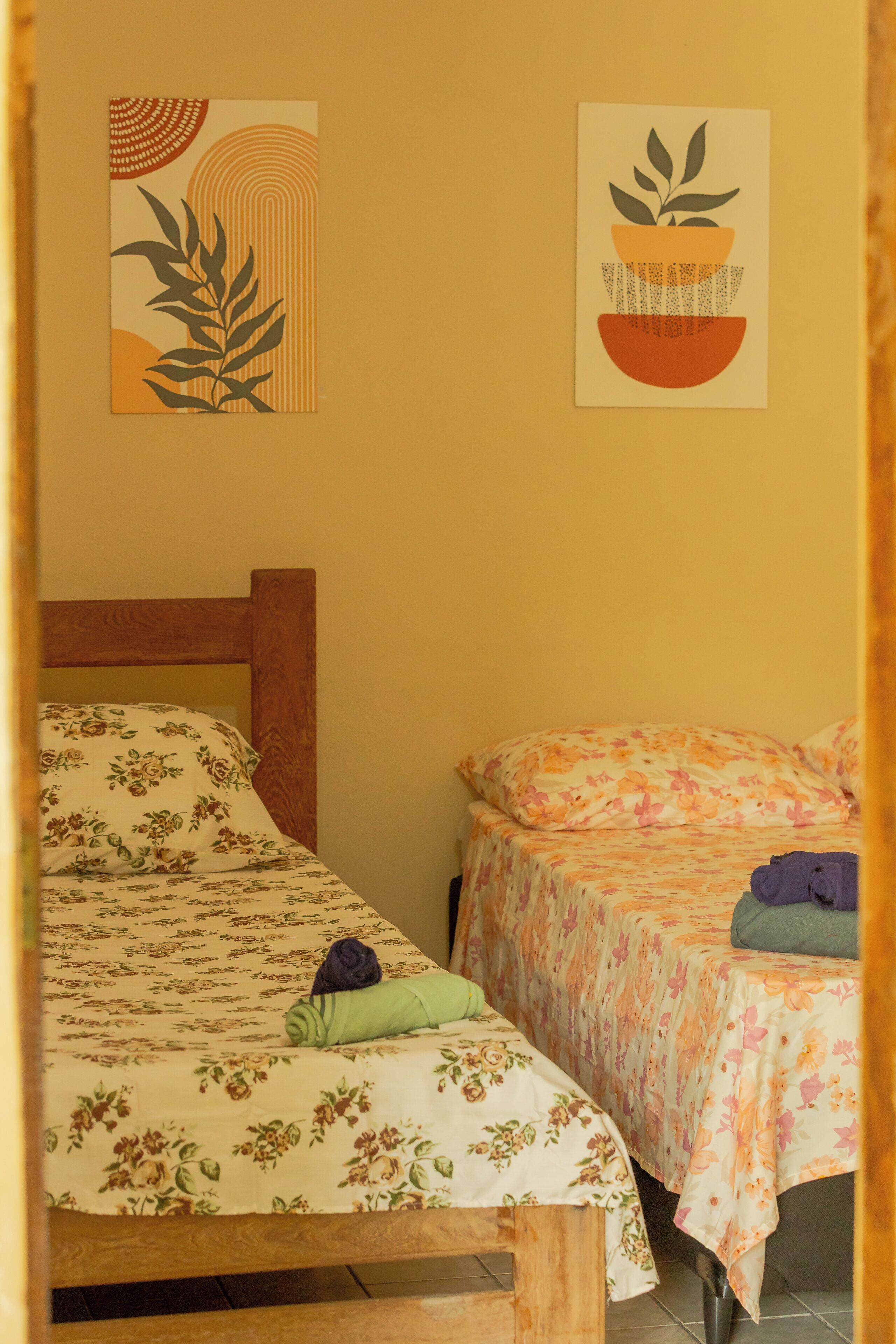 A room with two beds, each with floral bedding, a wooden headboard, and a green towel on one bed.
