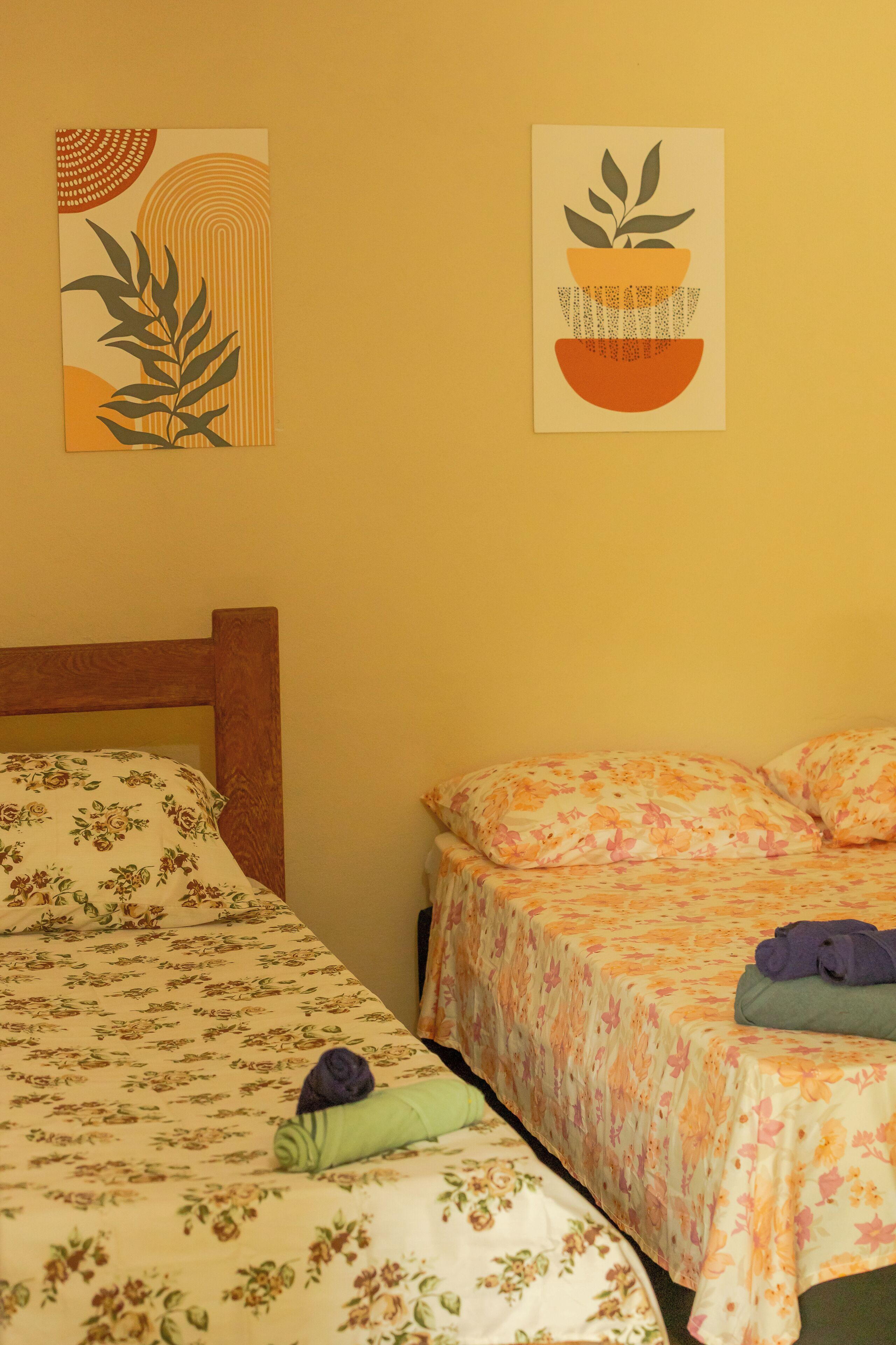 A room with two beds, floral bedding, and two wall-mounted artworks.