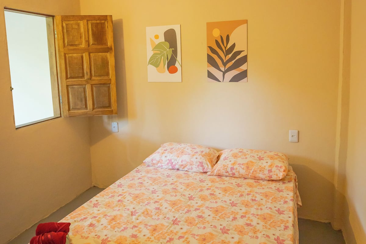 A small, single-bed room with a floral bedspread, a wooden door, and two wall art pieces.