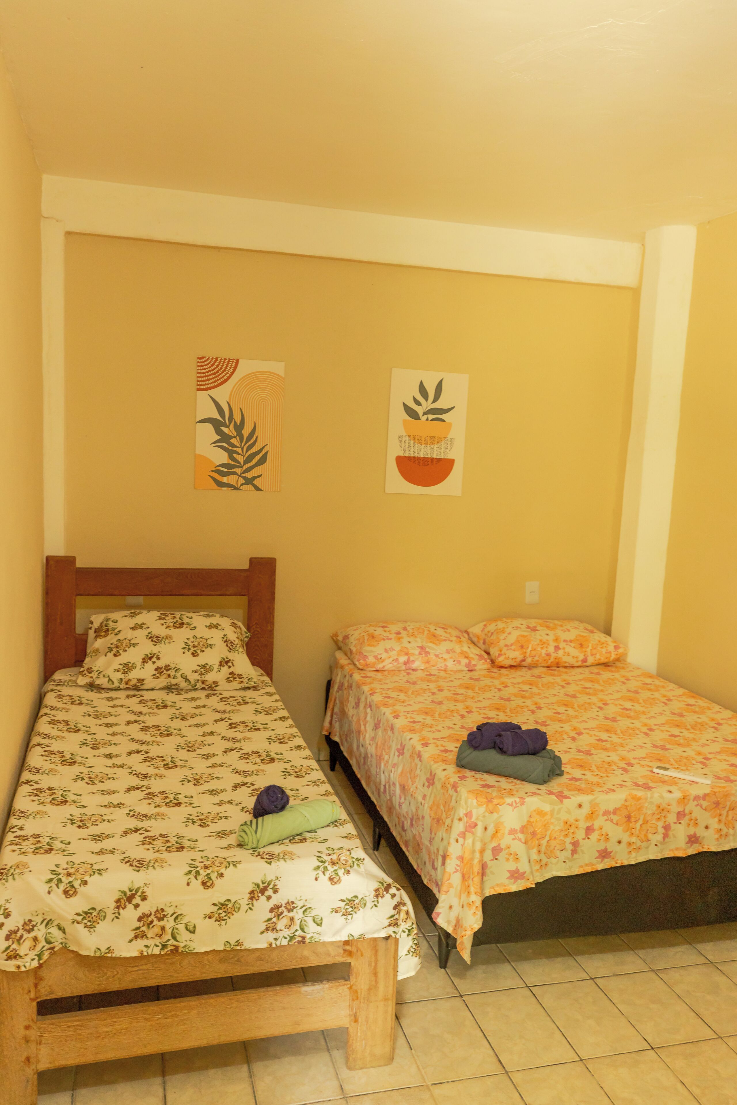 A room with two beds, each with floral bedding, a wooden headboard, and a small table with a purple item on it.