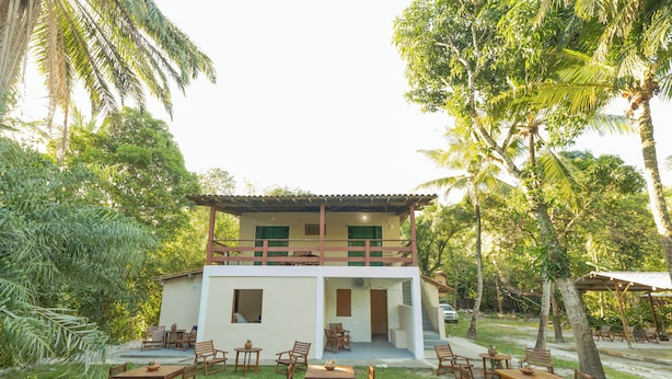 A two-story building with a balcony, surrounded by lush greenery and palm trees. - Pousada Raízes da Mata (Santa Cruz Cabrália)