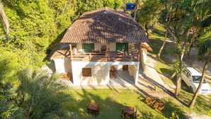 A two-story house with a tiled roof, surrounded by lush greenery and palm trees. - Pousada Raízes da Mata (Santa Cruz Cabrália)