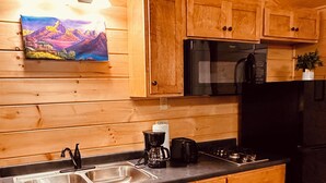 Eine Küchenzeile im Holzblockhaus-Stil mit doppelter Spüle, Herd, Mikrowelle und Kaffeemaschine.