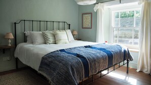 A bedroom with a bed, bedside lamps, a window with curtains, and a wall-mounted picture.